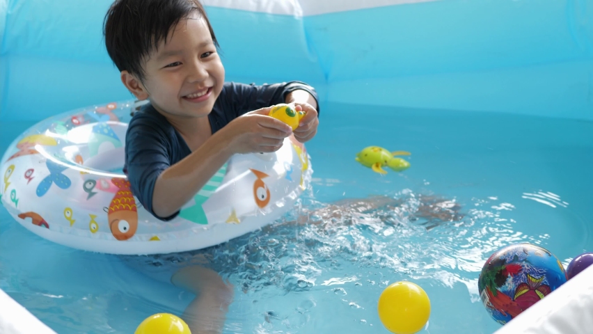 Asian cute child boy playing water in blue pool at home, laughing with happy relaxing face. Concept of family activity at home, freedom fun, sport time, summer.
