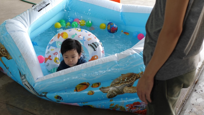 Asian cute child boy playing water in pool at home, laughing with relaxing face. Concept of family activity at home, freedom fun, father day, togetherness, relationship.