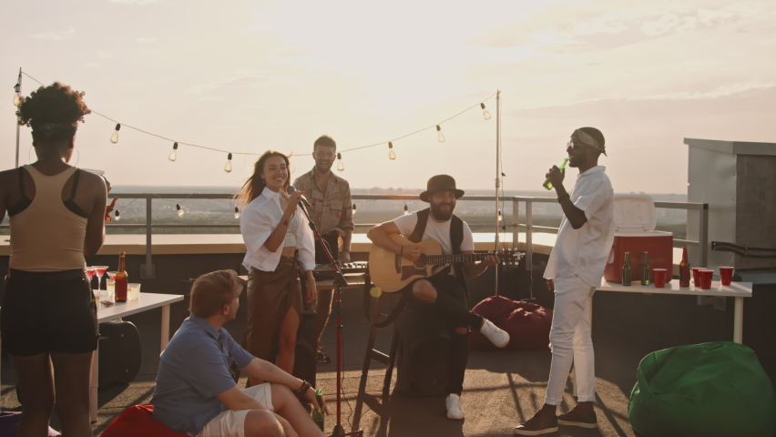 Handheld tracking shot of band playing music at party on rooftop terrace on windy summer evening | Shutterstock HD Video #1076653157