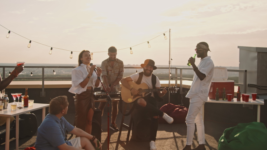 Handheld tracking shot of band playing music at party on rooftop terrace on windy summer evening | Shutterstock HD Video #1076653157