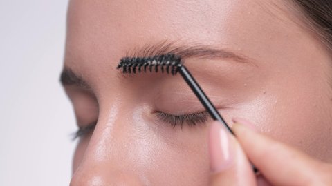 The make-up artist combs the eyebrows and makes the styling of the eyebrows with a gel. 
 Professional makeup and facial care.