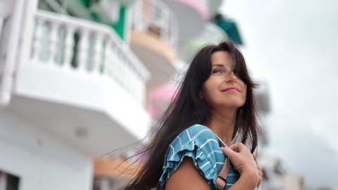 Happy relaxed brunette travel lady walking on street of touristic city enjoying summer vacation slow motion. Smiling young elegant woman tourist relaxing outdoor at architecture balcony facade hotel 