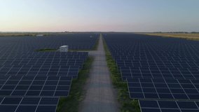 Aerial drone view into large solar panels at a solar farm at sunny summer evening. Solar cell power plants, green grass. Footage video 4k.