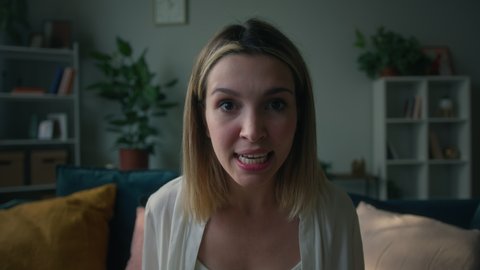 Aggressive emotional young woman shouting, portrait of screaming female person sitting on sofa in living room, looking in camera and swinging her arms, feeling anger and stress, bad mood.