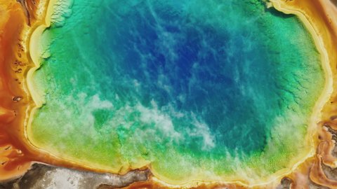 Close up scenic steam rises up above cinematic clear vibrant blue, green water of colorful rainbow lake waters. Beautiful landscape of volcano geyser at Yellowstone National park, 4K aerial footage