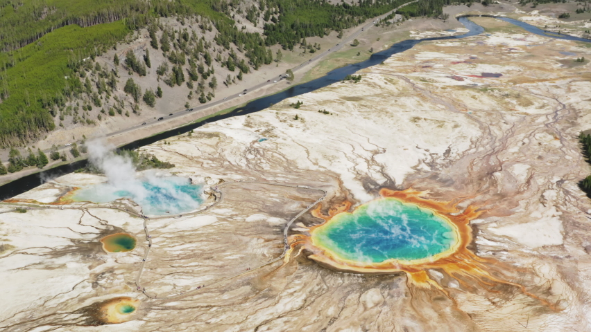 Helicopter aerial view of first American National park - Travel Yellowstone concept footage, 4K aerial. Tourists walking at steaming vibrant blue, green, teal, rainbow geyser lakes at Grand Prismatic Royalty-Free Stock Footage #1076674256