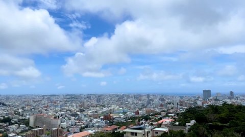 NAHA, OKINAWA, JAPAN - JUNE 2021 : Aerial high angle wide view of Naha city in daytime. Sunny summer blue sky and clouds. Cityscape of downtown area. Time lapse shot. Holiday and travel concept.