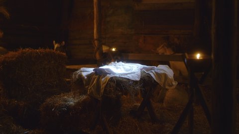 Zoom in view of white sheet placed in illuminated manger prepared for baby Jesus Christ in dark inn barn in Bethlehem nativity scene
