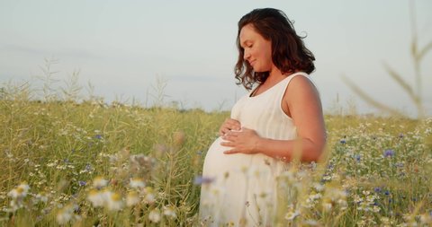 Pregnant woman with a big belly feeling happy outdoors. Adult expecting mother stroking belly on nature.  Middle age white pregnant woman touching her belly while sunset. Woman pregnancy concept.