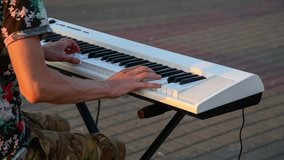 Close-up view of male street performer playing on white digital piano on city square at sunset. 4K resolution video. Music theme.