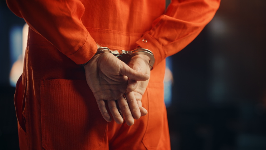 Cinematic Close Up Footage of a Handcuffed Convict at a Law and Justice Court Trial. Handcuffs on Accused Criminal in Orange Jail Jumpsuit. Law Offender Sentenced to Serve Jail Time.