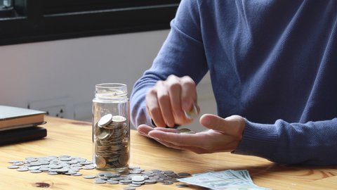 Man puts a coin dollar in a jar, Saving money for future growth and knowing how to manage your spending wisely, Saving money for business growth or long-term profitability.