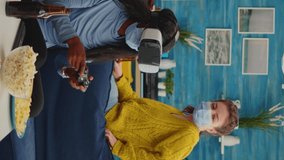 Vertical video: Mixed group of people guiding black woman with vr headset playing virtual video games in living room keeping social distancing agaist covid19. Diverse friends having fun at new normal - Powered by Shutterstock - Get 15% off with code: PIKWIZARD15
