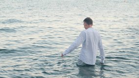 A man walks into the sea wearing clothes, back view - Powered by Shutterstock - Get 15% off with code: PIKWIZARD15