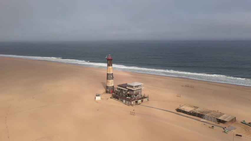 Flight over the oceanfront lighthouse at Sandwich Harbour in Namibia, Africa. UHD 4k drone video footage Royalty-Free Stock Footage #1076698787