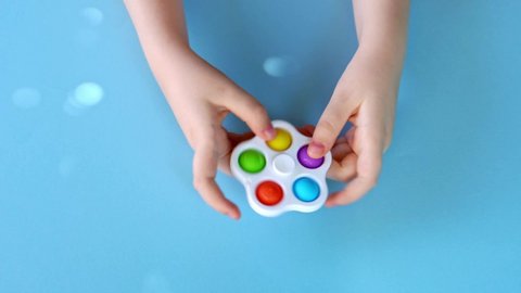 Top view of a children hands playing with Simple Dimple spinner on bright blue background. Silicone anti-stress sensory toy. Simple dimple reusable stress relief toy.