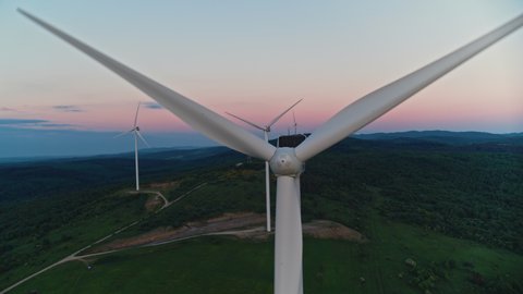 Aerial view of huge wind farm with working turbines on green field. Summer sunset on background. Alternative energy concept.