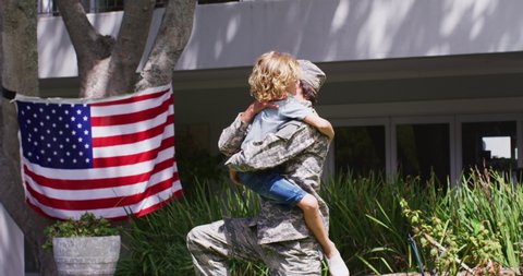 Caucasian son hugging his military dad in uniform in the garden. veteran soldier returning home concept