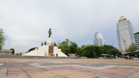 BANGKOK - MAY 04, 2018: The King Rama VI Monument at entrance to Lumpini park, establishing shot. Unidentified woman pass by at side of tiled square, green trees and two towers seen on background