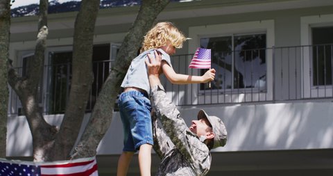 Caucasian son holding american flag hugging his military dad in uniform in the garden. veteran soldier returning home concept