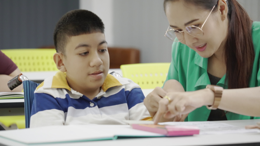 Handicap boy in wheelchair practicing writing with  woman teacher in classroom. School for children with autism. Education helps develop skills for children. confidence activities Royalty-Free Stock Footage #1076708897