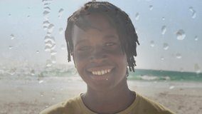 Animation of smiling african american man at sunny beach over droplets. happy holidays and free time, digitally generated video. digitally generated video.