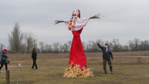 Zaporizhzhia, Ukraine - March 13, 2021: Slavic holiday Maslenitsa. Pagan doll against the gray sky. Idol for the holiday. Pancake Festival. The wind blows ribbons. Motanka doll prepared for burning