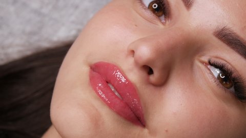 Beautiful young woman with permanent lip make up and microblading eyebrow tattoo lies with a beauty parlor after the procedure. Close-up girl face