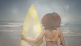 Animation of african american woman holding surfboard at sunny beach over lights. happy holidays and free time, digitally generated video.