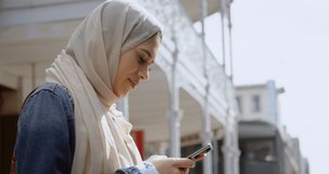 Animation of asian woman in hijab sitting and using smartphone over cityscape. communication technology and keeping in touch, digitally generated video.