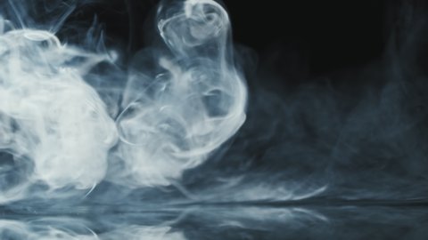 Slowmo close up of wisps of smoke flowing against black background and falling down on mirrored surface