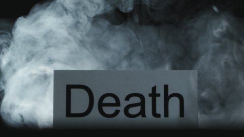 Close up isolated on black background shot of wisps of smoke flowing around sign with word Death on it. Concept of dangerous hobby