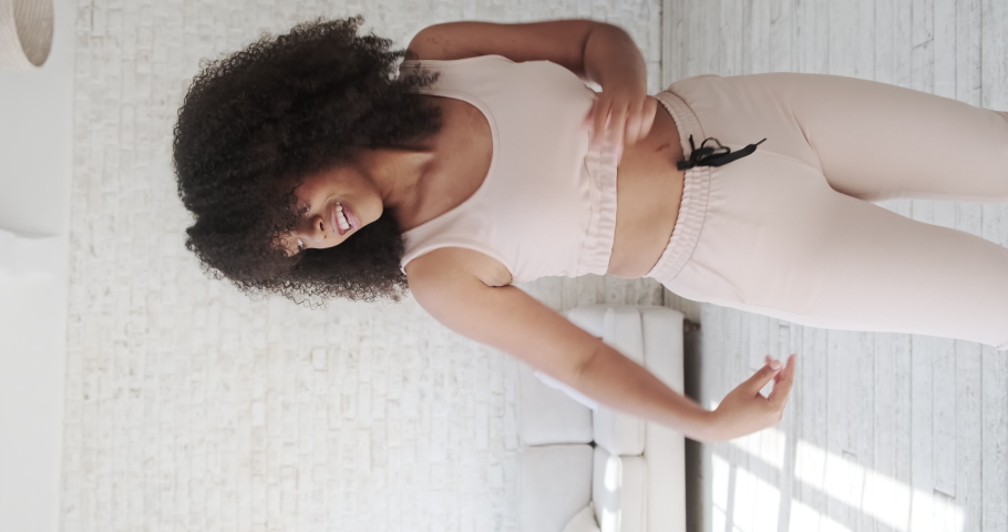Trendy happy black mixed race woman vlogger listeng music, dances and recording videostream video for social media at home. Creating dancing video using tiktok app. Vertical video. Royalty-Free Stock Footage #1076719175