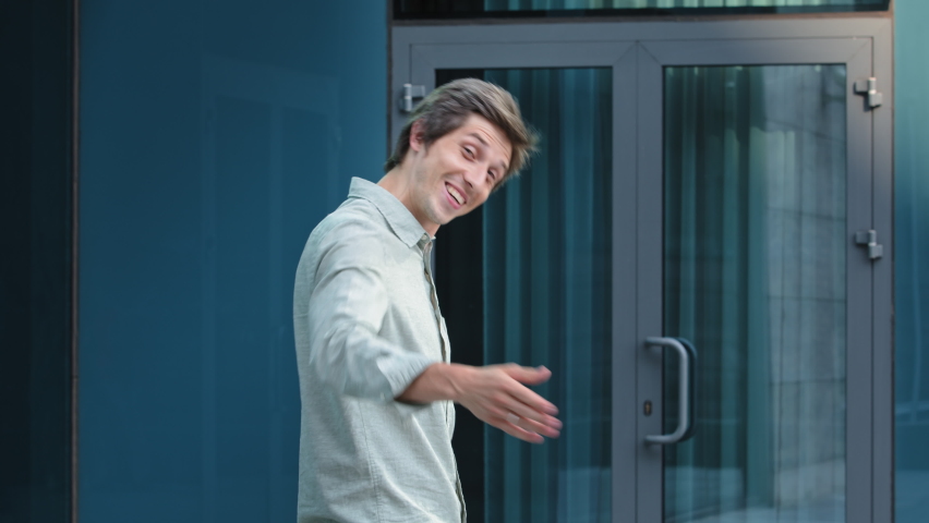 Portrait of smiling successful friendly young man in formal attire standing by door, hr recruiter stretching hand to camera glad to offer you job in company, greeting spectator as new workforce member | Shutterstock HD Video #1076721584