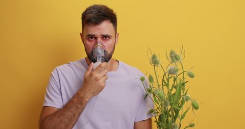 Sick man has chronic asthma makes inhalation at home wears oxygen respiratory mask to breath well has allergic reaction to pollen isolated over yellow background. Allergy attack. Breathing problems