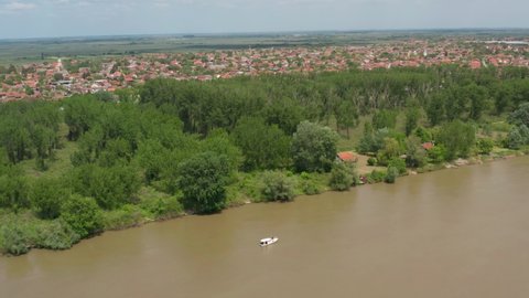 Aerial: boat travelling along murky river in Serbian city