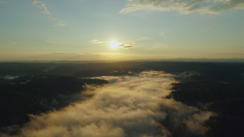 Aerial sunrise drone shot as sun burns fog from away from forest river valley, 4K