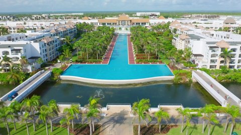 Aerial flyover natural pond, luxury swimming pool, palm trees in garden and expensive apartments of hard rock hotel resort in Punta Cana