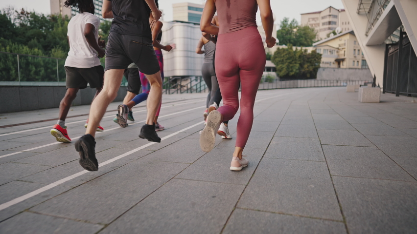 Multiracial team of like-minded people running through the city streets. People in sports uniforms and shoes have a group workout. Running club. Royalty-Free Stock Footage #1076730179