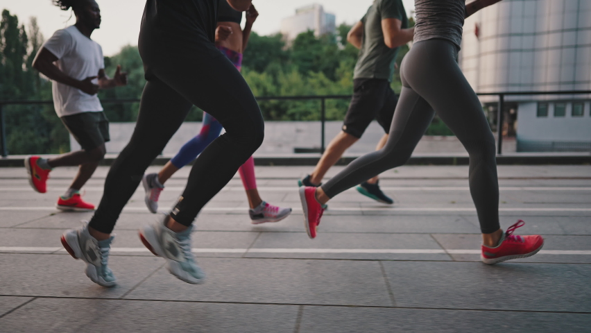 Multiracial team of like-minded people running through the city streets. People in sports uniforms and shoes have a group workout. Running club. | Shutterstock HD Video #1076730179