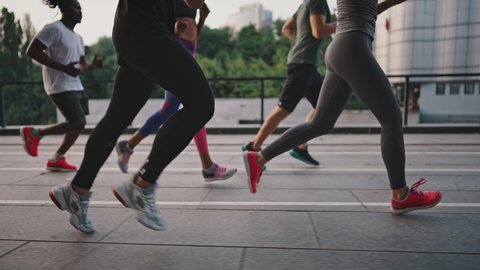 Multiracial team of like-minded people running through the city streets. People in sports uniforms and shoes have a group workout. Running club.