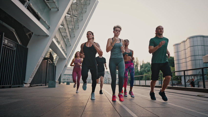 Running club. Multiracial team of like-minded people running through the city streets. People in sports uniforms and shoes have a group workout. Royalty-Free Stock Footage #1076730188