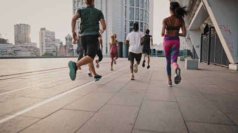 Big team of athletes has a group training session on the urban streets of a big city. A group of people jogging together at sunrise.