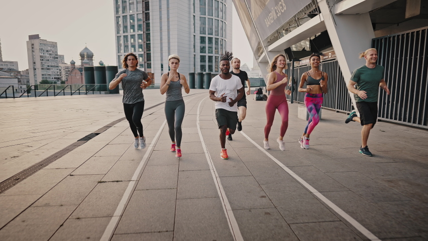 Front view. Running club, group of like-minded people run early in the morning at dawn along the urban streets. Multiethnic team of men and women training running before marathon, active life. Royalty-Free Stock Footage #1076730236