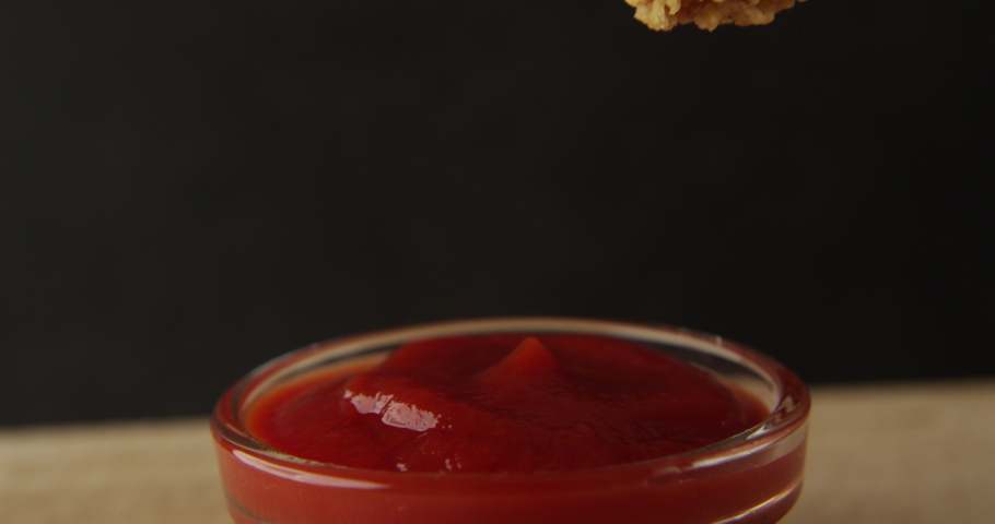 Chicken Wing is Dipped into a Ketchup Bowl on a Table with Black Background a Macro Shot Royalty-Free Stock Footage #1076734865