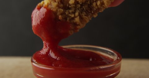 Chicken Wing is Dipped into a Ketchup Bowl on a Table with Black Background a Macro Shot