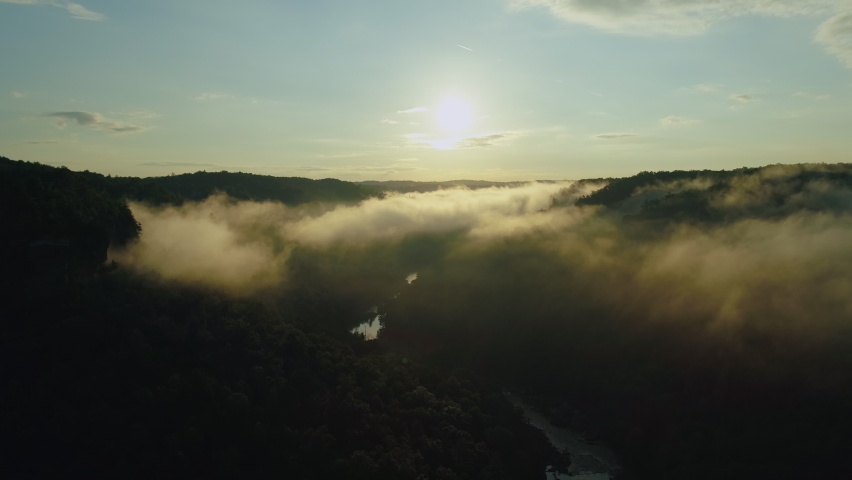 Aerial drone shot slowly rising up out of fog filled forest river valley, 4K