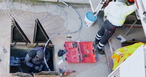 Modugno, Italy - December 2020: Workers insert fiber optic cables into the underground cable ducts to create a broadband telecommunications network. Open triangular cast iron manhole covers