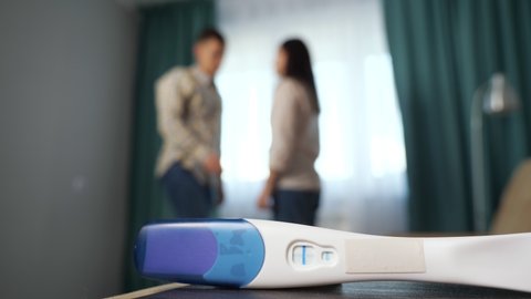 Close-up of positive pregnancy test with happy couple in the background.
