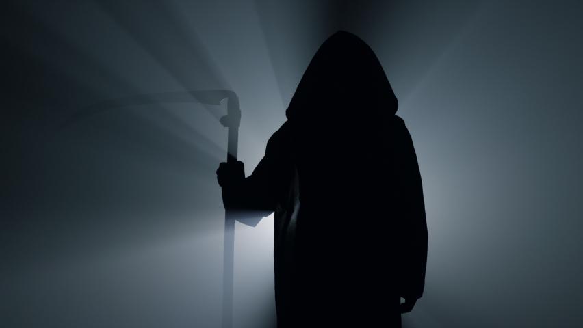 Silhouette of black robe person depicting death holding scythe indoors. Terrible grim reaper standing in darkness. Awful scytheman waiting in spotlight background. Halloween characters concept. | Shutterstock HD Video #1076743307